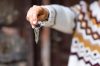 Caucasian hand of woman in winter sweater holding house keys in front to the wooden door.