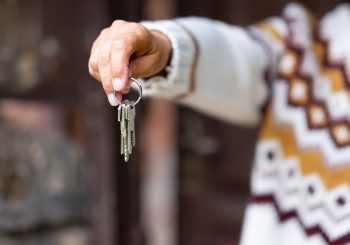 Caucasian hand of woman in winter sweater holding house keys in front to the wooden door.