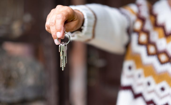 Caucasian hand of woman in winter sweater holding house keys in front to the wooden door.