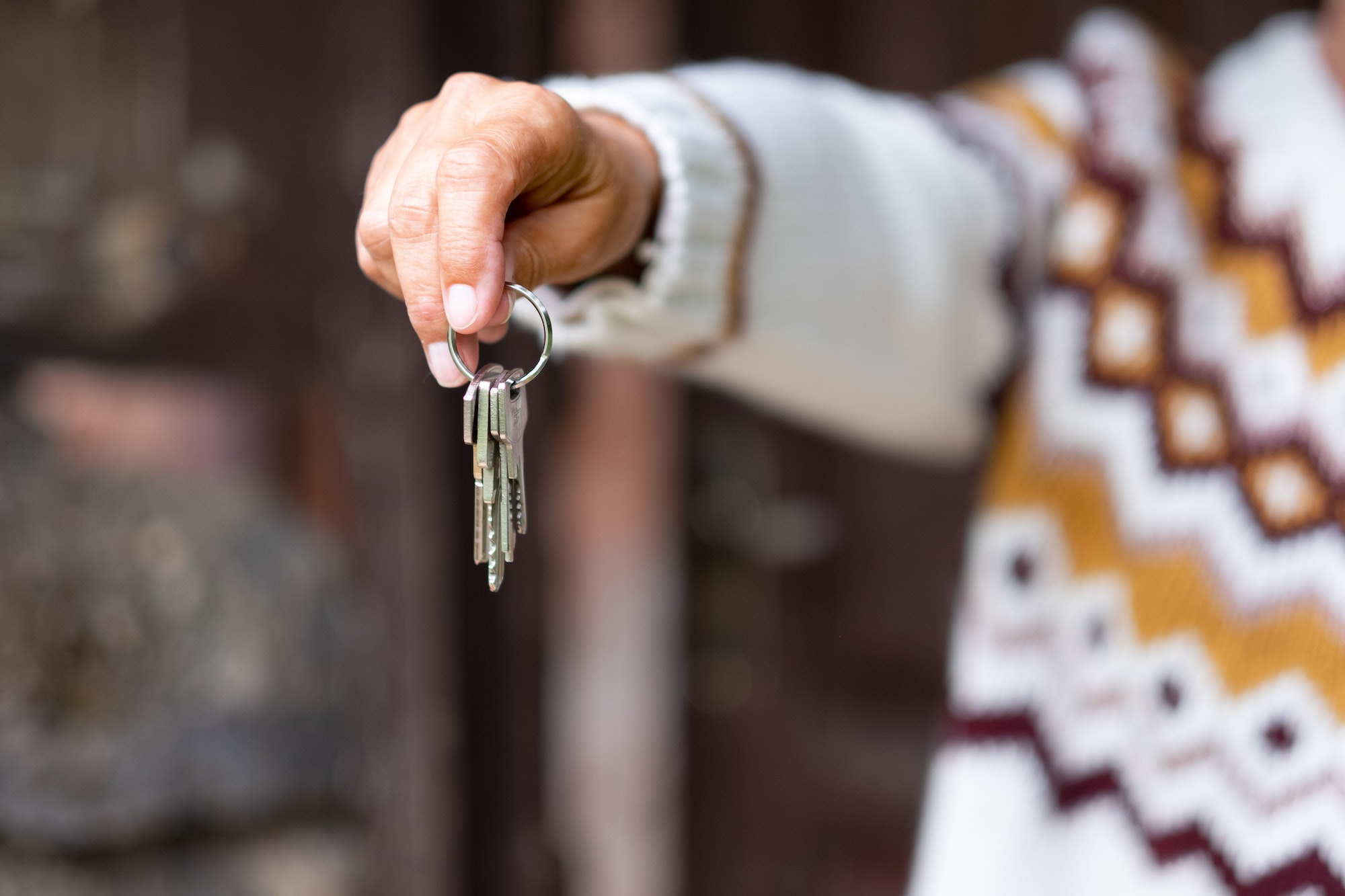 Caucasian hand of woman in winter sweater holding house keys in front to the wooden door.